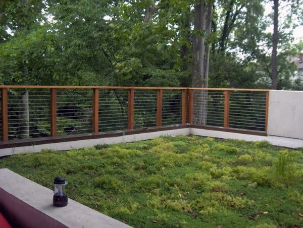 Wood and cable fence enclosing a lush green backyard area with surrounding trees.
