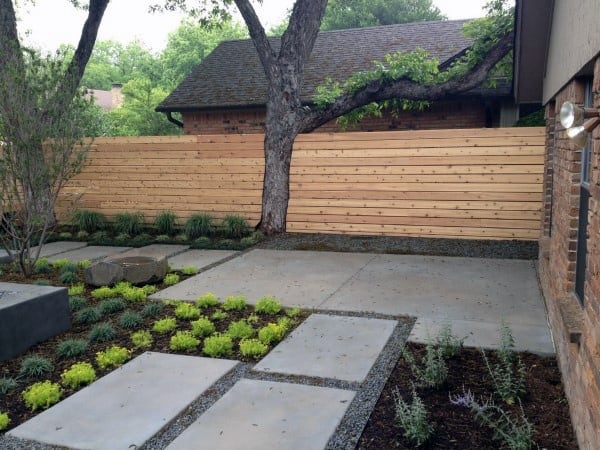 Horizontal wooden fence surrounding a landscaped backyard with concrete pavers and greenery.