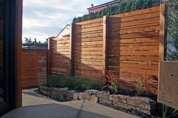Horizontal wooden fence with a raised stone planter bed and ornamental grasses in a modern backyard.