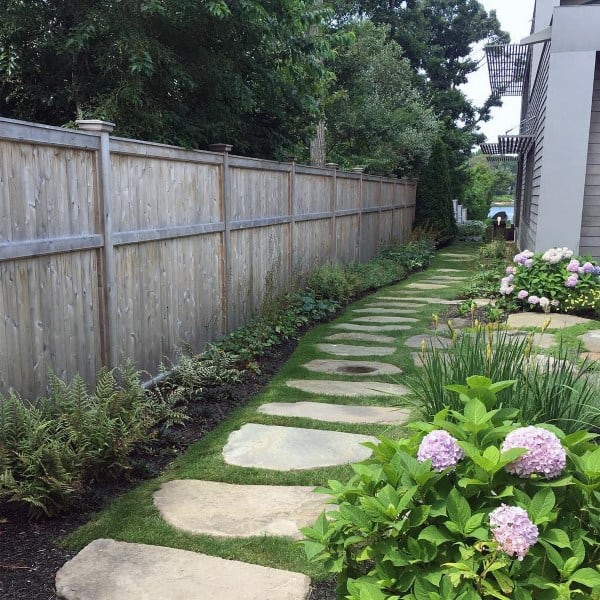 Wooden privacy fence alongside a stone path with ferns and hydrangeas in a garden.