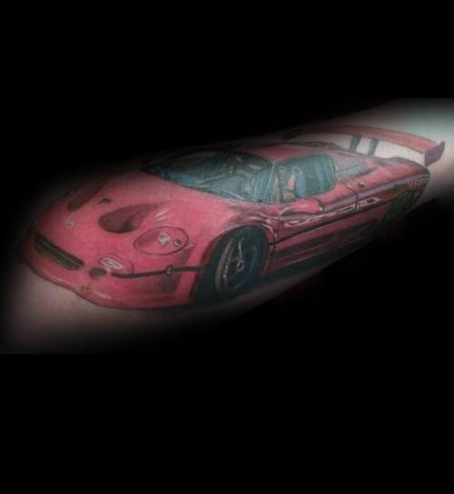 Detailed red Ferrari sports car tattoo on man's forearm, showcasing sleek design and passion for high-performance vehicles.
