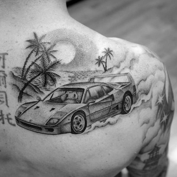 Black-and-grey Ferrari F40 tattoo on man's shoulder, set against tropical palm trees and sun, evoking freedom and adventure.
