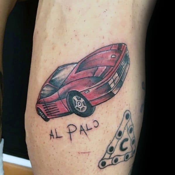 Simple Ferrari Testarossa tattoo with "Al Palo" text on man's leg, expressing classic style and personal passion for cars.
