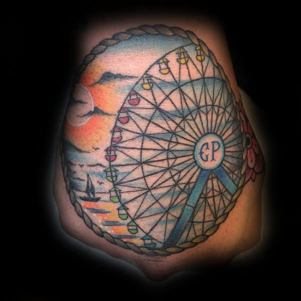 Colorful Ferris wheel tattoo with a sunset beach scene, framed by a rope border, featuring soft shading and vibrant details for a nautical feel.