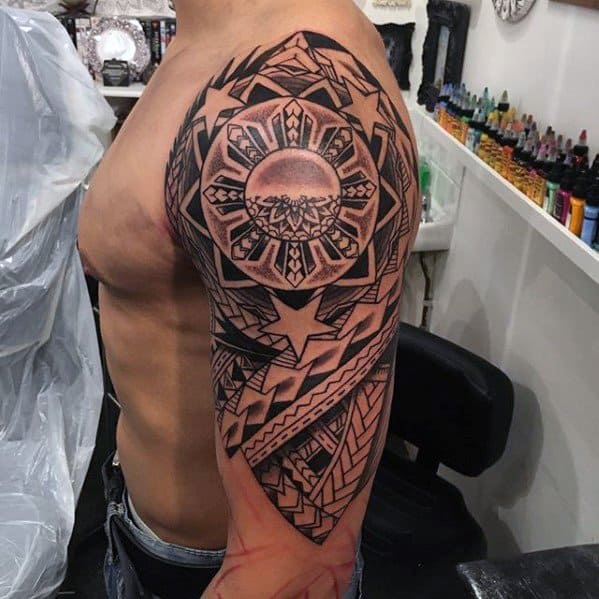 Filipino sun tattoo on the upper arm with tribal patterns, detailed rays, and a large central sun surrounded by bold star and weave elements.