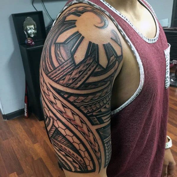 Upper arm Filipino sun tattoo featuring bold tribal rays, curved geometric lines, and intricate woven patterns forming a dynamic half-sleeve.