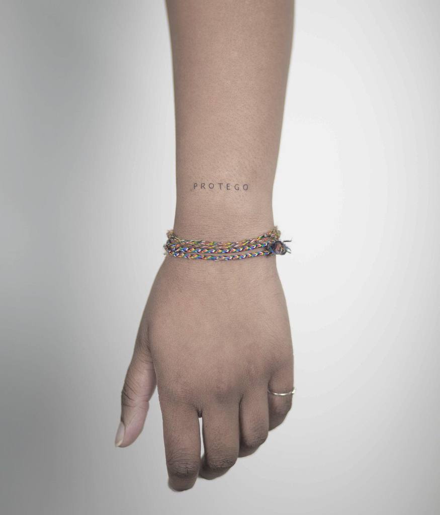 Minimalist Harry Potter tattoo of the word 'PROTEGO' in small, simple font, symbolizing the protective spell