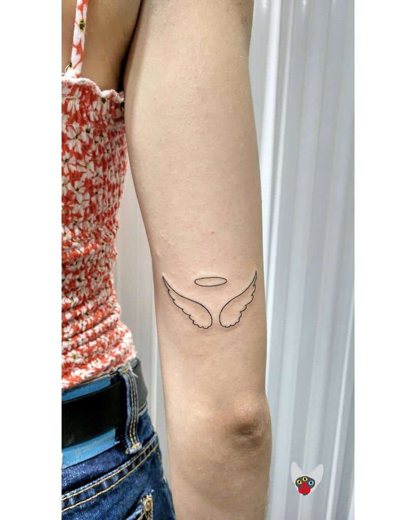 A minimalist angel wings tattoo with a halo symbolizing purity, protection, and spirituality in fine line design