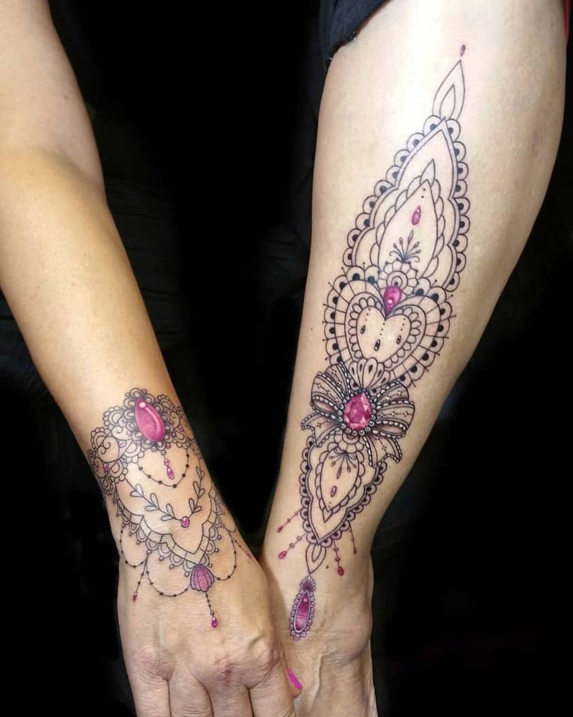 Elegant lace-inspired forearm and wrist tattoos featuring intricate patterns, delicate beadwork, and pink gemstone details for a jewelry effect.