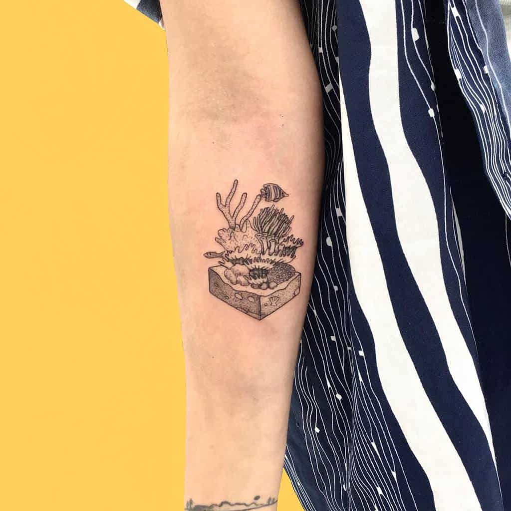 Minimalist coral reef tattoo, featuring detailed coral, anemones, and a small fish emerging from a cube-shaped ocean base