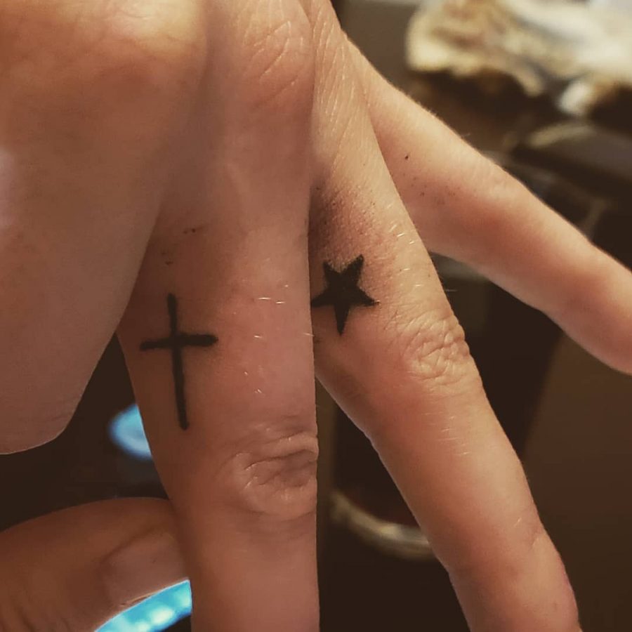 Close-up of hands with star tattoo on one finger and cross tattoo on another