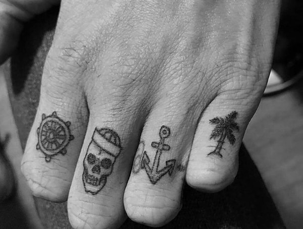 Close-up of fingers with tattoos: ship wheel, skull with hat, anchor, and palm tree