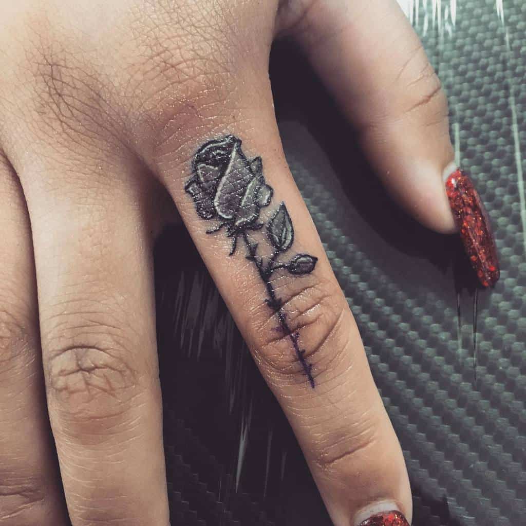 A hand with a black rose tattoo on the finger