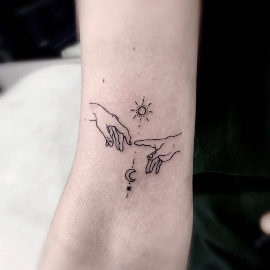 Minimalist black ink tattoo of two hands reaching towards each other, with a sun above and a crescent moon below, symbolizing balance and connection.