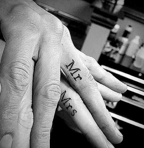 Matching finger tattoos reading “Mr.” and “Mrs.” on ring fingers, symbolizing marriage, unity, and a lifelong commitment.