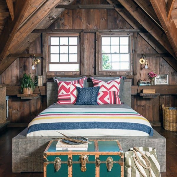 Cozy attic bedroom with wooden walls, vibrant bedding, and a vintage trunk at the foot of the bed