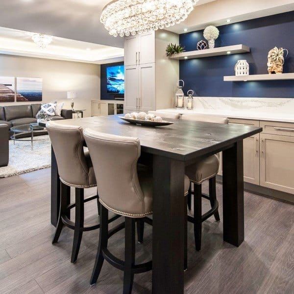 Modern basement dining area with crystal chandelier, bar seating, and decorative shelving.