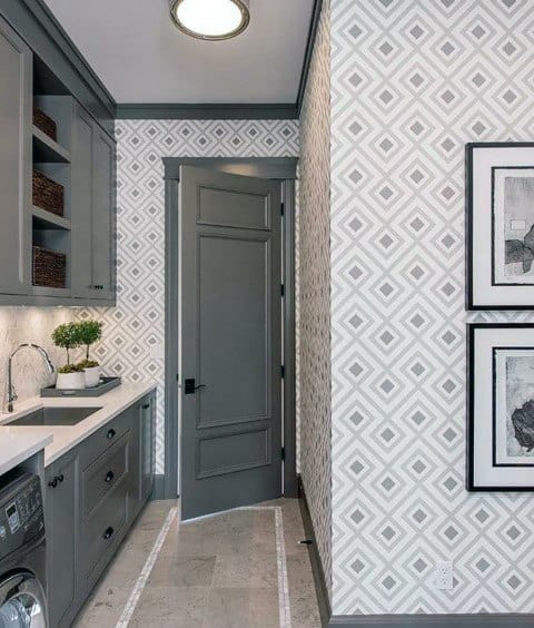 Stylish laundry room with gray cabinets, geometric wallpaper, and framed wall art.