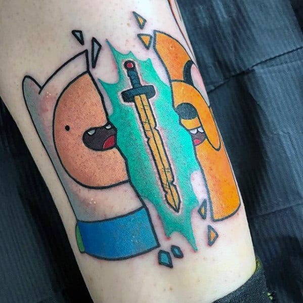 Adventure Time tattoo of Finn and Jake split by a glowing sword in the center with shattered glass effect, inked on the forearm.