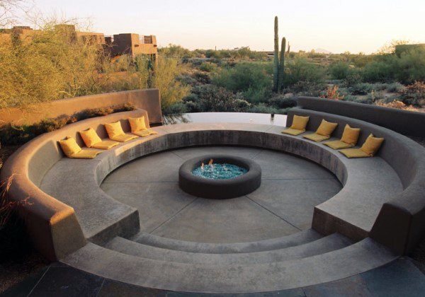 Circular outdoor seating with yellow cushions, a central fire pit, and desert landscape framed by cacti