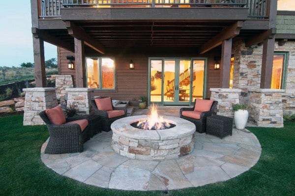 Cozy patio with cushioned wicker chairs surrounds a stone fire pit beneath a wooden balcony