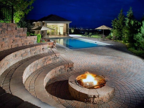 Backyard with a cozy fire pit, steps, pool, and a view of a well-lit modern house at night