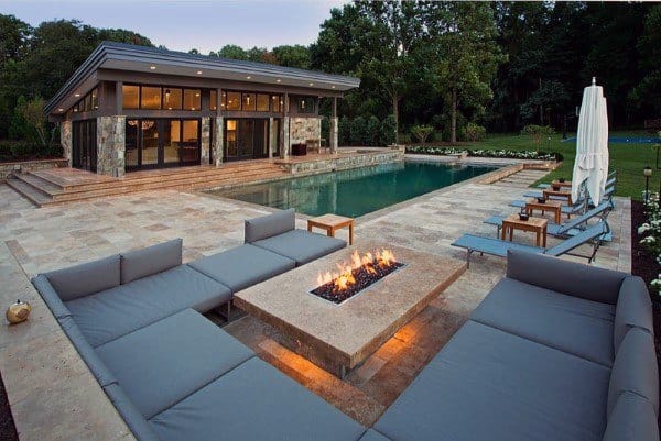 Luxurious backyard with a pool, modern patio furniture, a cozy fire pit, surrounded by greenery and a sleek house