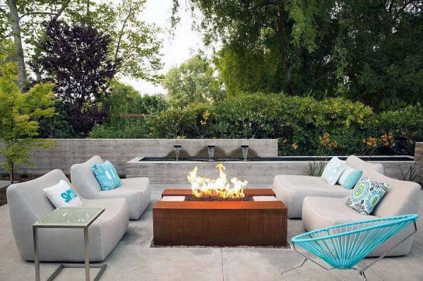 Modern patio with gray sofas, fire pit, blue chair, and lush greenery in the background