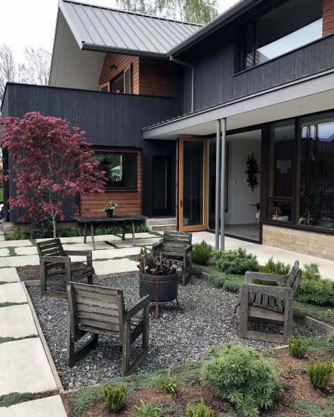 Modern house with a metal roof, featuring a garden patio with wooden chairs and a small tree