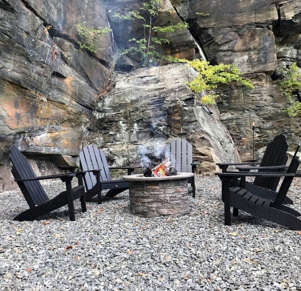 Four chairs around a fire pit on a rocky surface with large stone cliffs in the background