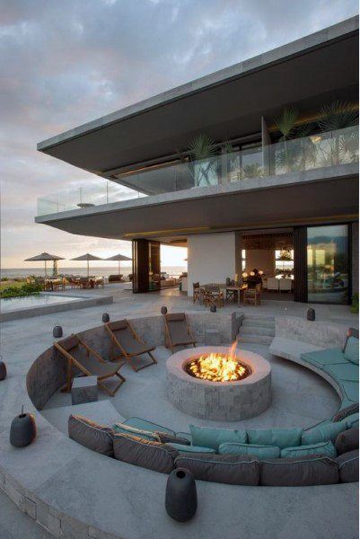 Outdoor patio with a fire pit, circular seating, and sun loungers, boasting beach and ocean views
