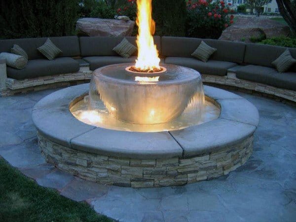 Curved cushioned bench encircles a round fire pit with a stunning waterfall feature