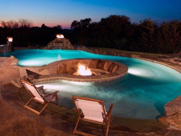 Luxurious outdoor pool at dusk with fire pits and cozy lounge chairs nearby