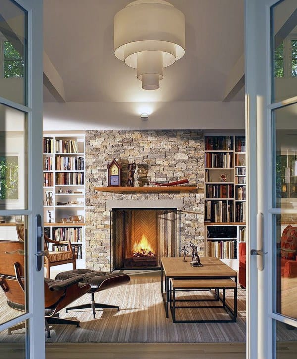 Cozy library with stone fireplace, wooden mantel, built-in bookshelves, and modern furniture.