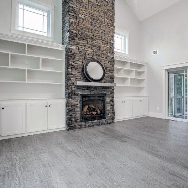 Modern living room with tall stone fireplace, built-in white shelving, and light wood flooring.
