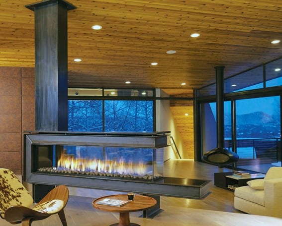 Modern suspended gas fireplace with glass enclosure and stone accents.