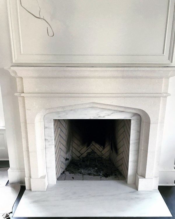 White marble fireplace with an arched surround, detailed mantel, and herringbone brick firebox.