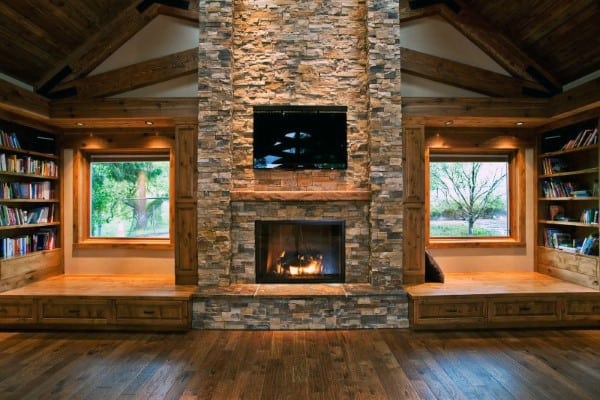 Cozy living room with stacked stone fireplace, built-in wooden bookshelves, and vaulted ceiling.