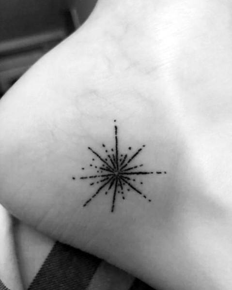Minimalist black ink firework tattoo with fine lines and dots, placed on the ankle for a subtle yet stylish and elegant design.