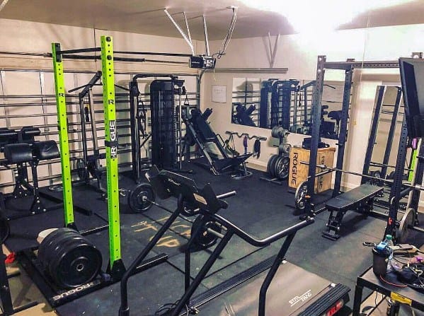 Garage gym with green squat rack, treadmill, weight machines, and mirrored walls for a modern setup.