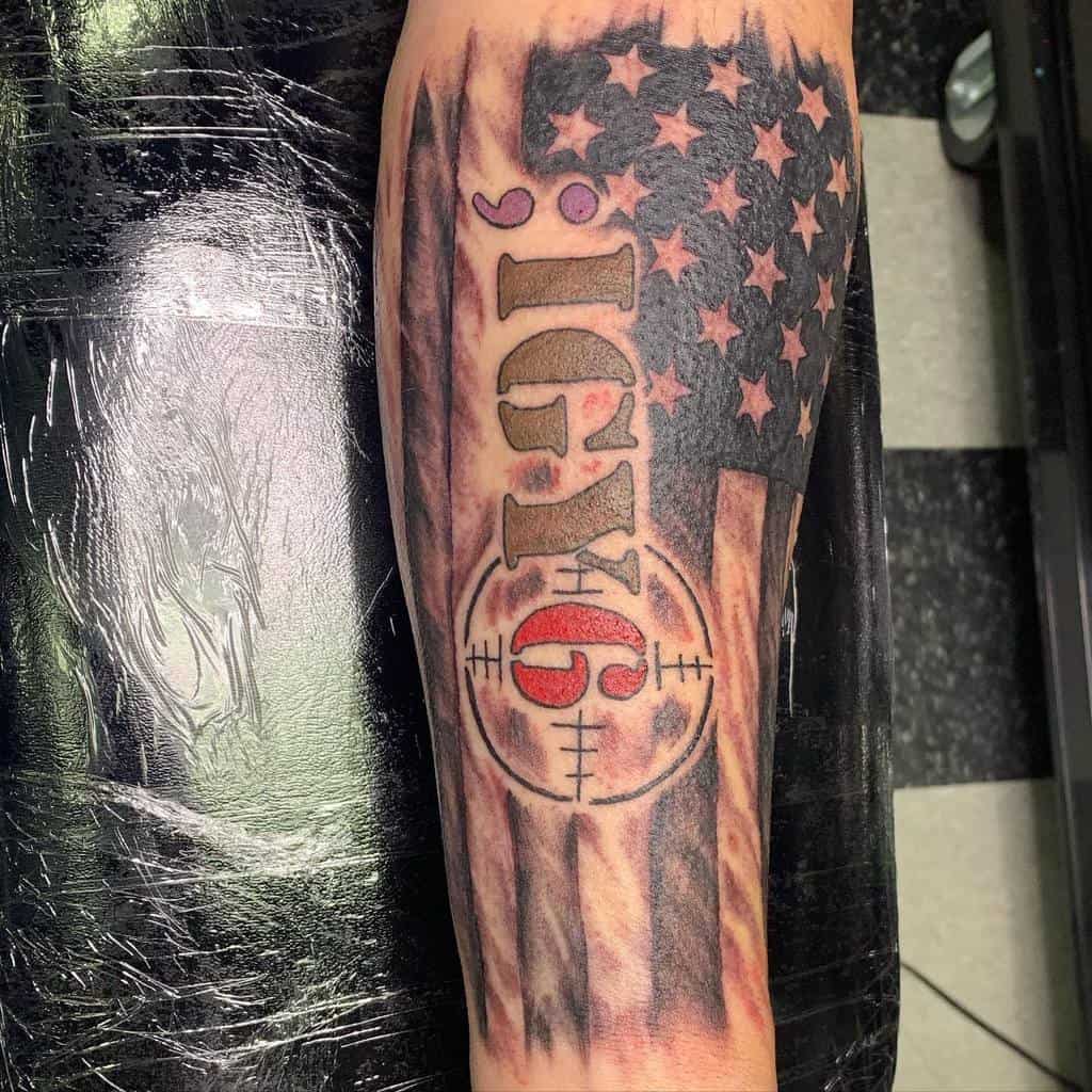 Forearm tattoo featuring ';IGY6' with an American flag background, red 6 in a crosshair design, symbolizing support and awareness