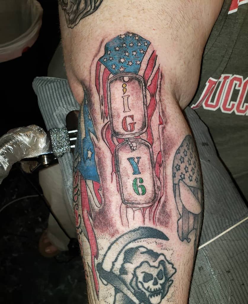 Arm tattoo featuring ';IGY6' on military dog tags with an American flag background, symbolizing service and remembrance