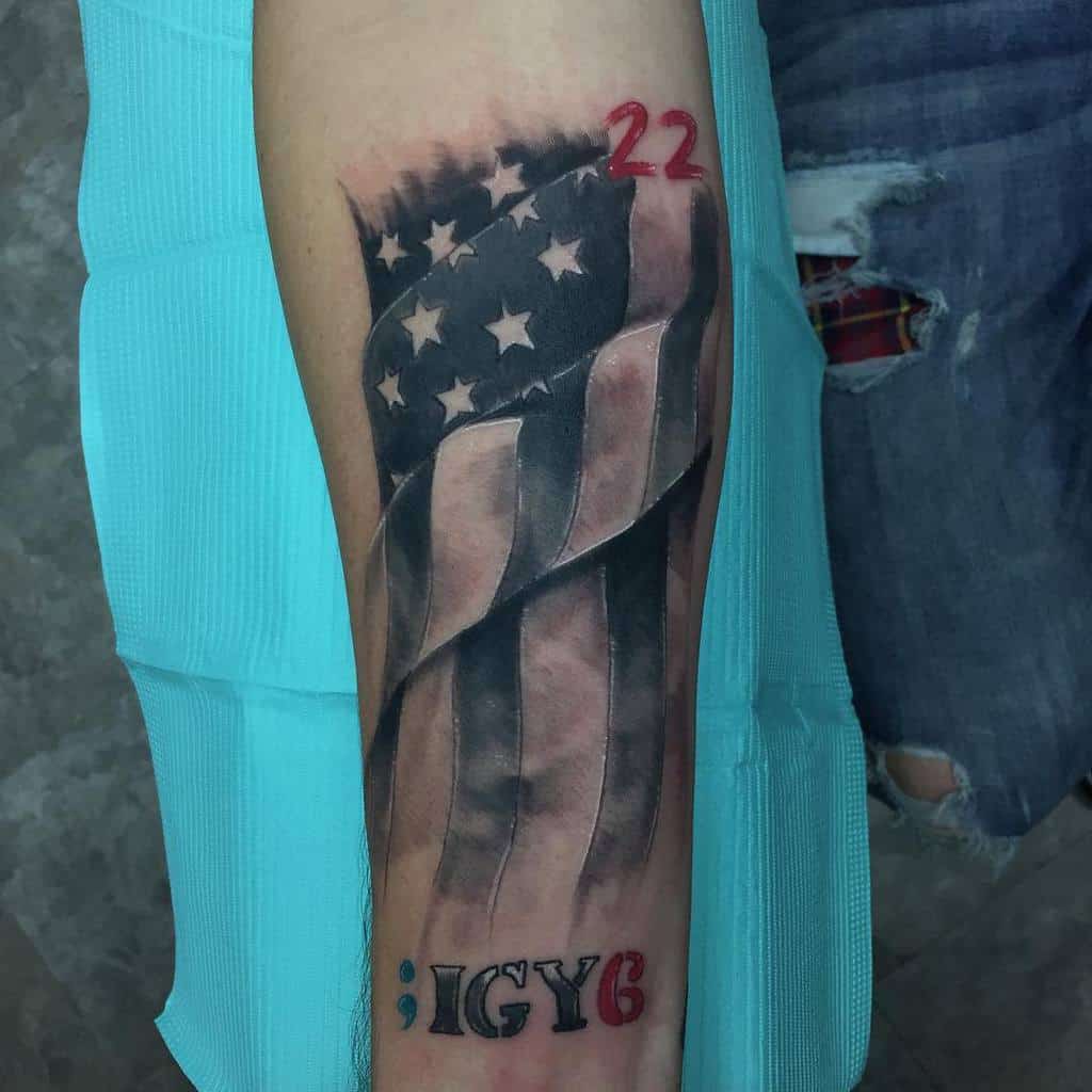 Tattoo of a shaded American flag with "22" in red ink and ";IGY6" at the bottom on an arm
