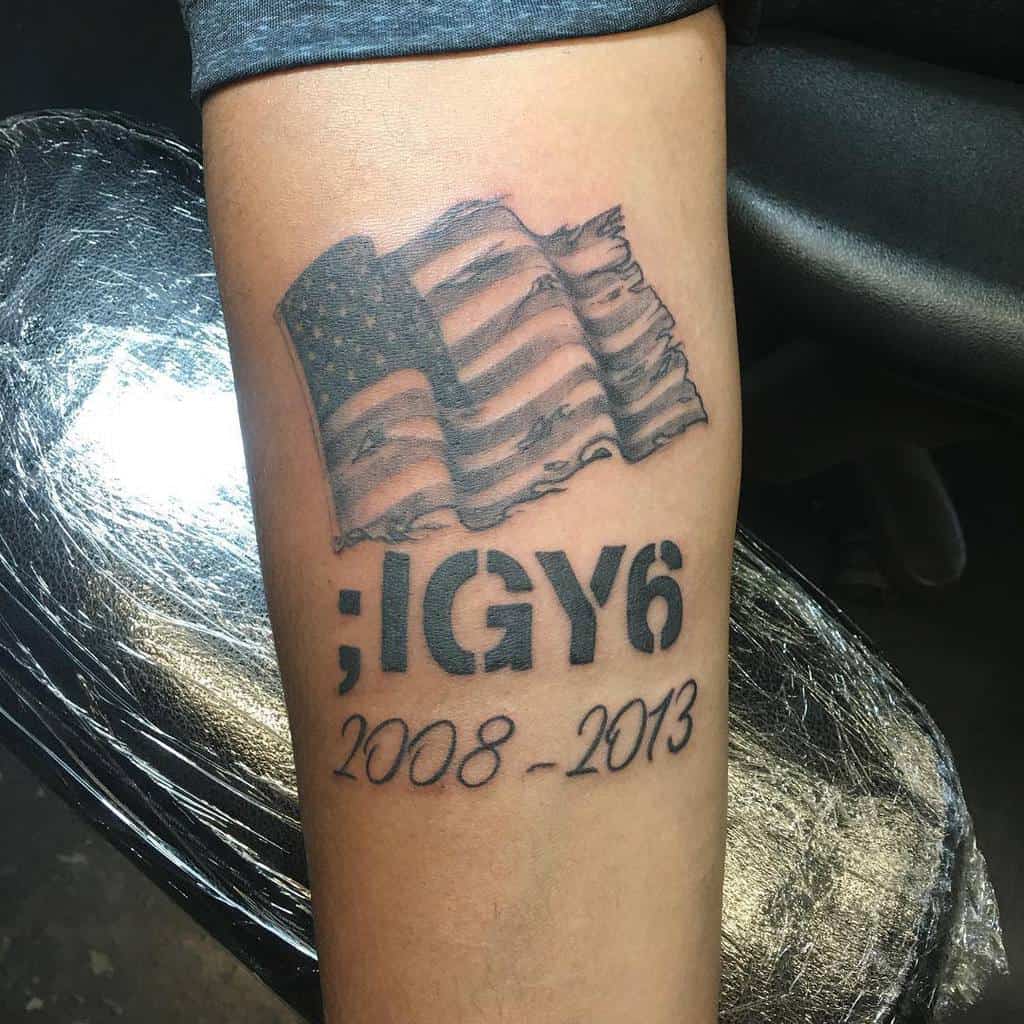 Tattoo of a tattered American flag with text ";IGY6" and "2008-2013" on a forearm
