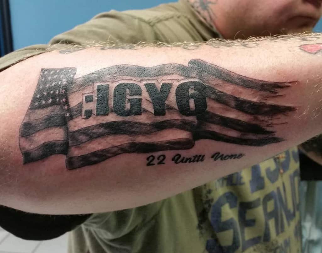 Tattoo of a tattered American flag with text ";IGY6" and "22 Until None" on a forearm