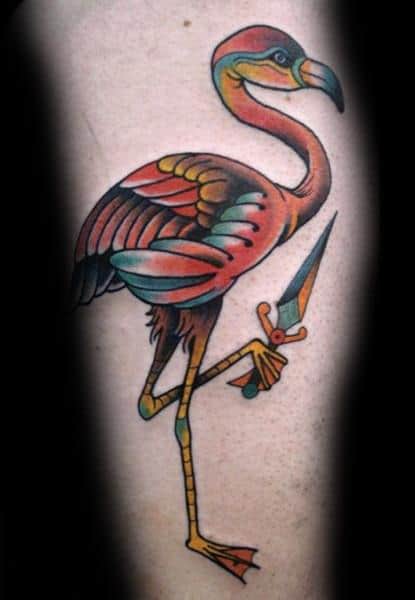 Neo-traditional flamingo tattoo with bold outlines, rich colors, and a dagger in its claw, creating a striking and edgy design.
