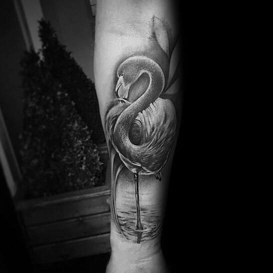 Realistic black and grey flamingo tattoo on the forearm, featuring fine shading and elegant reflection in water for a lifelike effect.