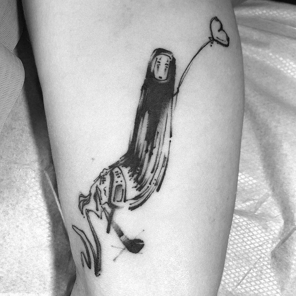Minimalist black ink tattoo of No-Face from Spirited Away, floating with a heart-shaped balloon, blending into abstract brush strokes