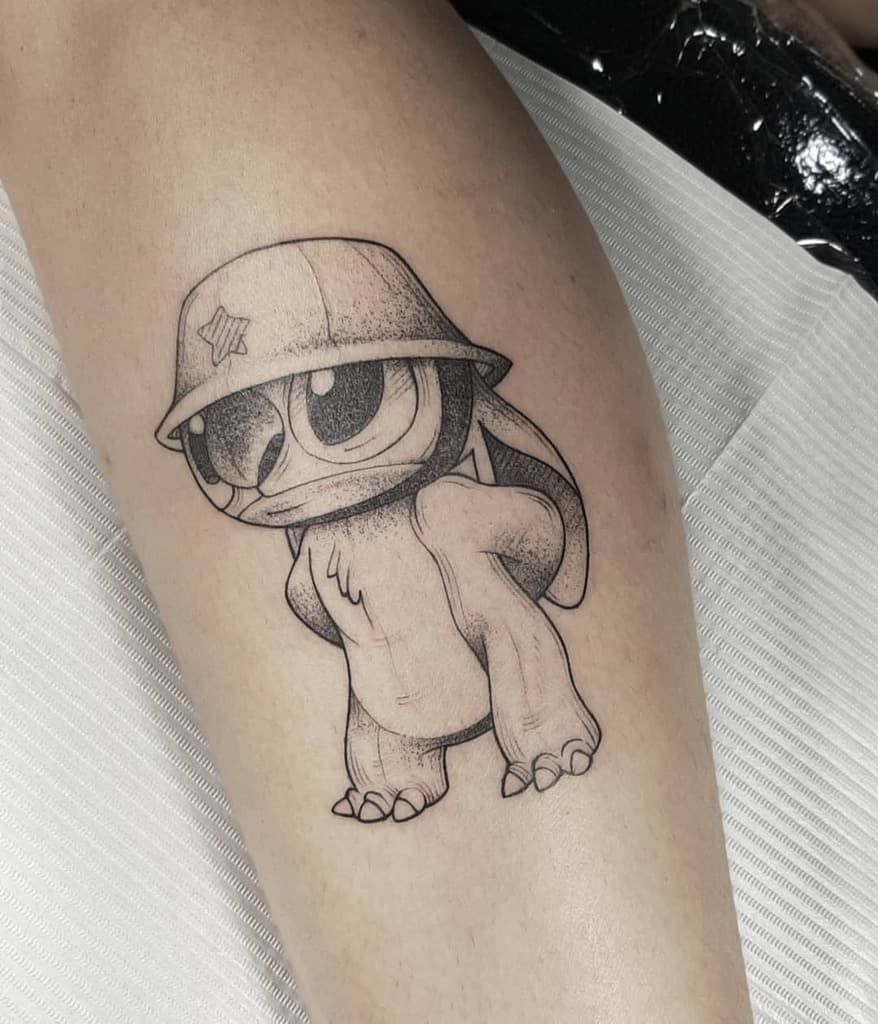 Black and gray tattoo of Stitch from Lilo & Stitch wearing a soldier's helmet, standing with a serious expression, on the arm.