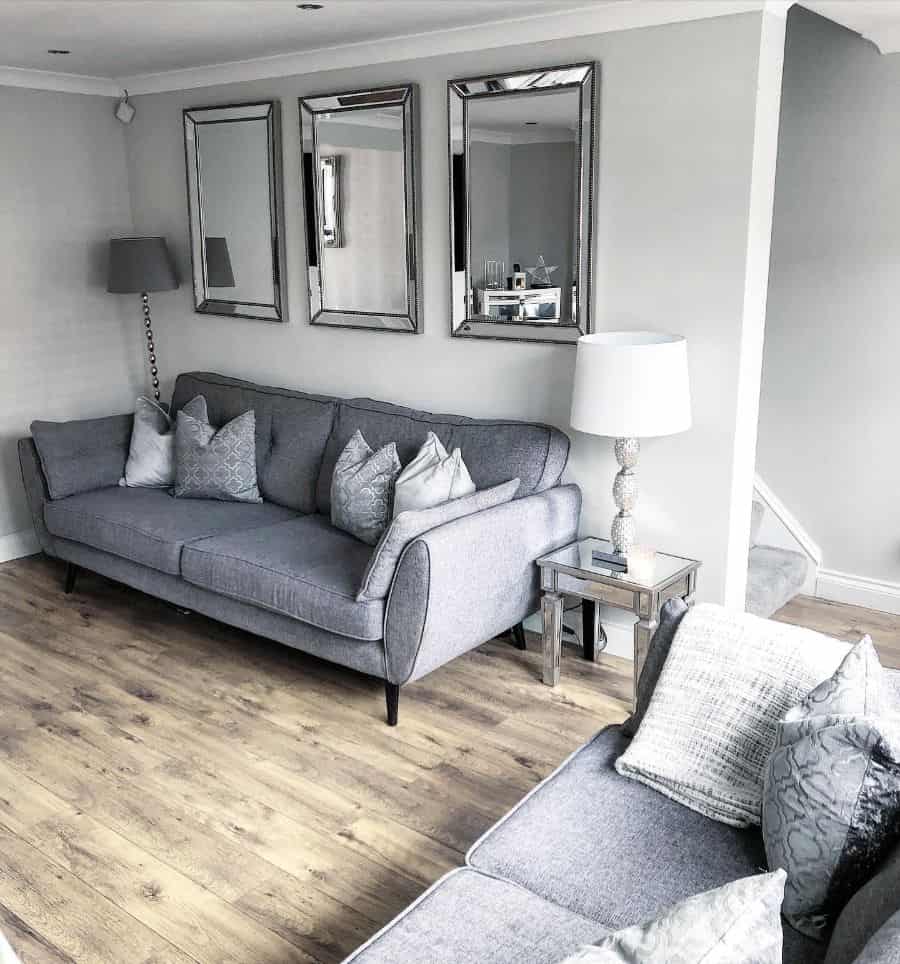 Modern living room with grey sofas, mirrored wall decor, wooden floors, and a neutral color scheme.